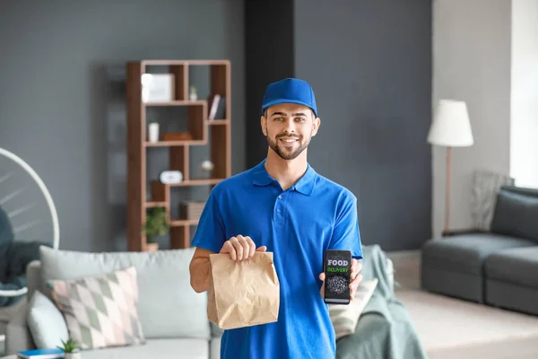 Handsome worker of food delivery service with mobile phone indoors — 스톡 사진