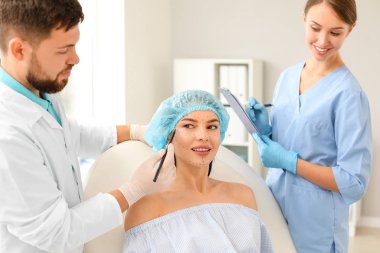 Klinikte hastanın yüzüne işaret uygulayan plastik cerrah