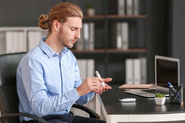 Diabetic man taking blood sample with lancet pen in office