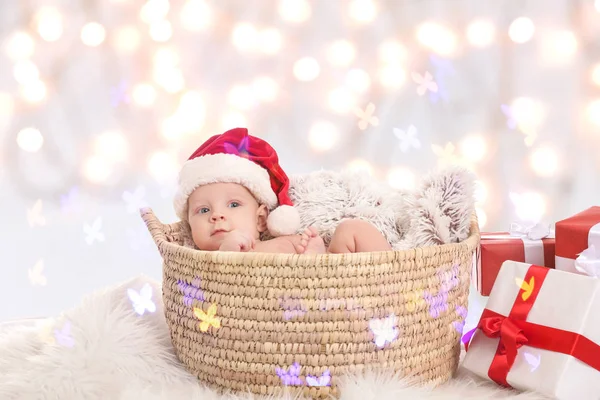 Bebê bonito com chapéu de Papai Noel deitado na cesta contra luzes de Natal borradas — Fotografia de Stock