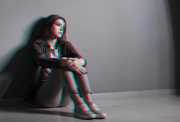 Depressed young woman sitting near grey wall — Stock Photo, Image