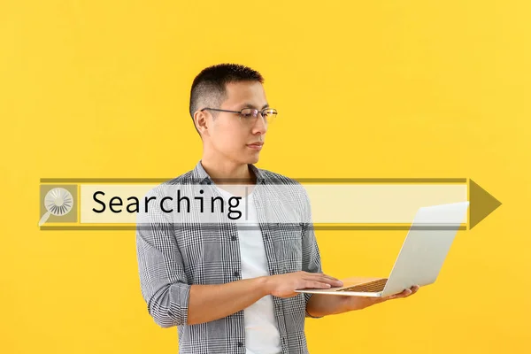 Asian man with laptop using web search engine against color background — Stock Photo, Image