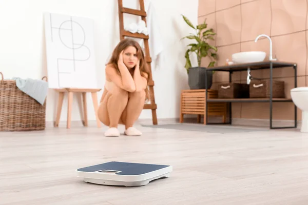 Sad young woman and scales in bathroom. Diet concept — Stock Photo, Image