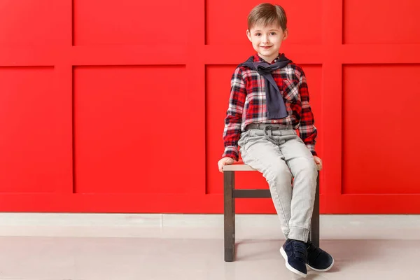 Cute little boy in autumn clothes sitting near color wall — Stock Photo, Image