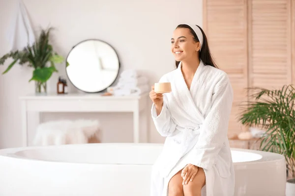 Mooie jonge vrouw drinken koffie in de badkamer — Stockfoto