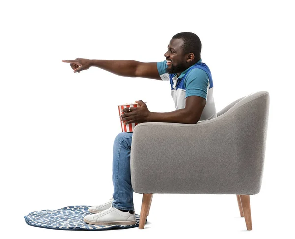 African-American man with popcorn watching TV while sitting in armchair against white background — Stock Photo, Image