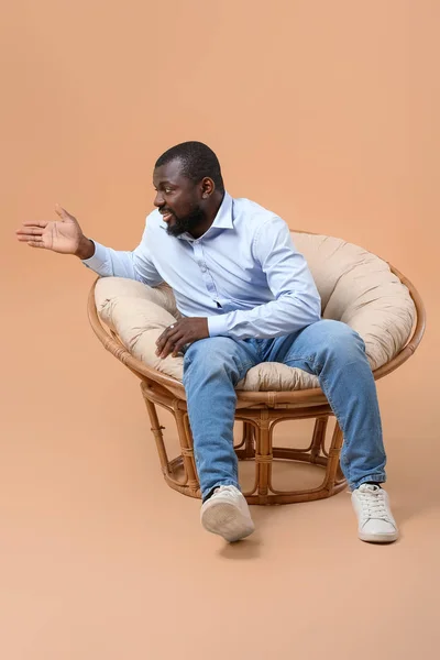 African-American man sitting in armchair against color background — Stock Photo, Image