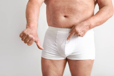 Ürolojik hastalığı olan olgun bir adam ışık arka planında baş parmağını aşağı gösteriyor.
