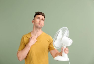 Young man with electric fan on color background