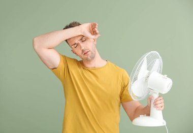 Young man with electric fan on color background