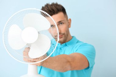 Young man with electric fan on color background
