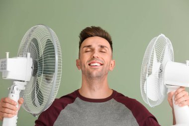 Young man with electric fans on color background clipart