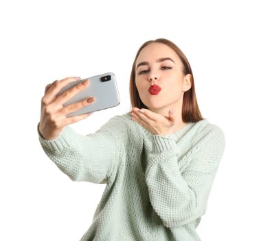 Güzel genç bir kadın beyaz arka planda selfie çekiyor.