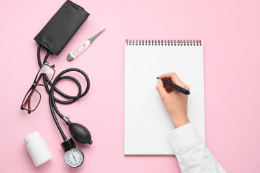 Not defterine, sphygmomanometreye ve renk arkaplanına haplar yazan doktorun eli