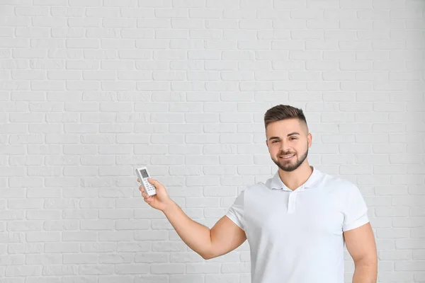 Young man with air conditioner remote control on light background — ストック写真