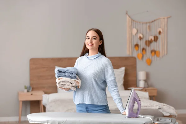 Beautiful young woman with clean ironing laundry at home — стоковое фото