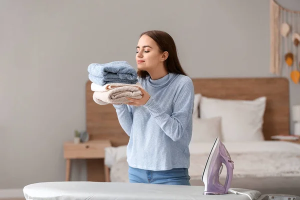 Beautiful young woman with clean ironed laundry at home — Stock Photo, Image