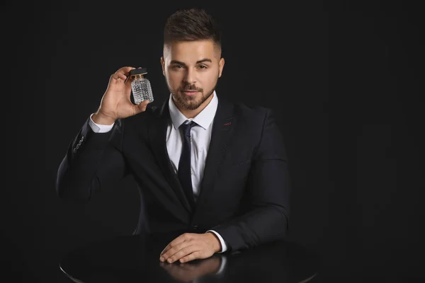 Joven guapo con botella de perfume sobre fondo oscuro —  Fotos de Stock