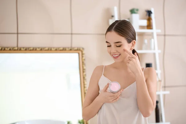 Hermosa mujer joven aplicando crema en su cara en el baño — Foto de Stock
