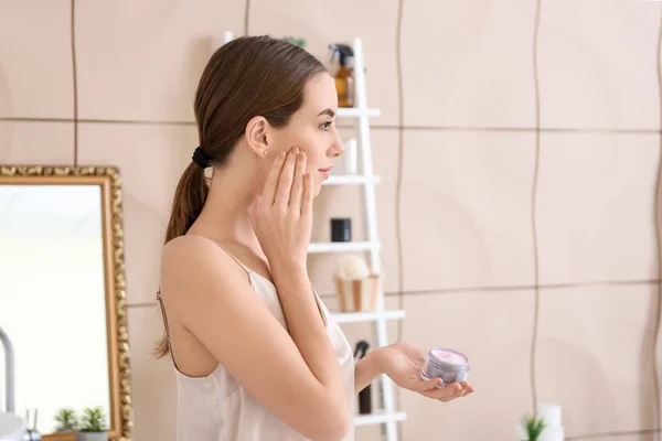 Mulher bonita aplicando creme em seu rosto no banheiro — Fotografia de Stock