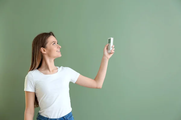 Mladá žena s klimatizací dálkové ovládání na barevném pozadí — Stock fotografie