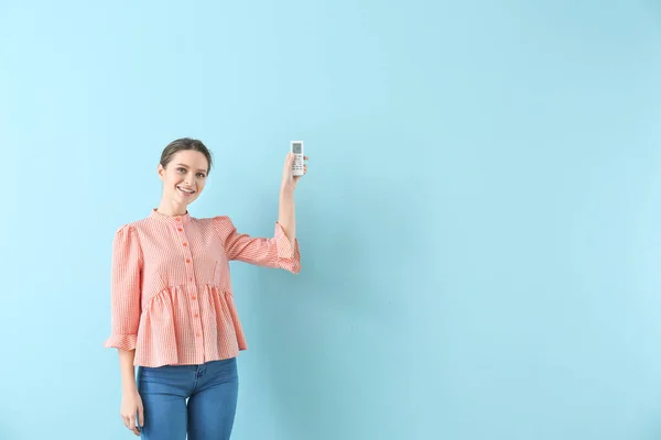 Giovane donna con aria condizionata telecomando su sfondo colore — Foto Stock