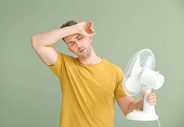 Young man with electric fan on color background — Stock Photo, Image