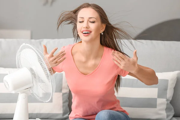Evde sıcak hava dalgası sırasında elektrikli yelpaze kullanan genç bir kadın. — Stok fotoğraf