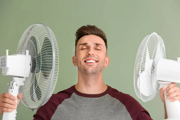 Young man with electric fans on color background