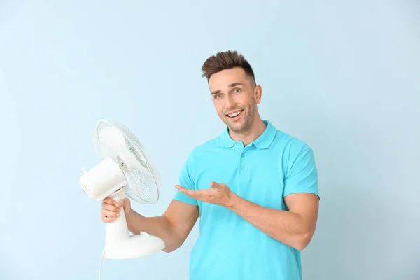 Young man with electric fan on color background — Stock Photo, Image
