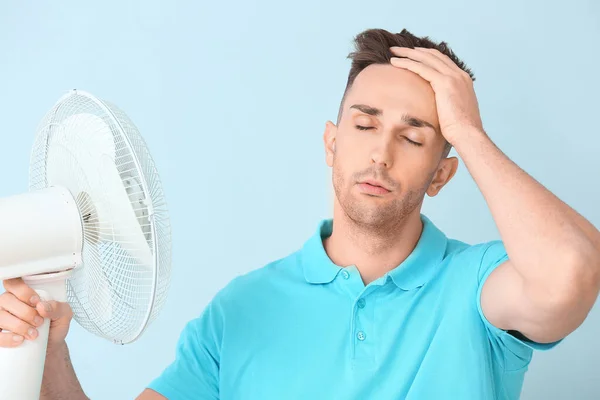 Joven con ventilador eléctrico sobre fondo de color —  Fotos de Stock