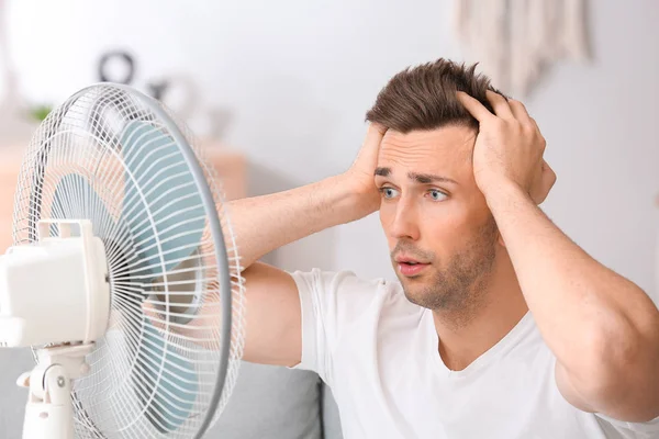 Shocked hombre cerca de ventilador eléctrico en casa —  Fotos de Stock