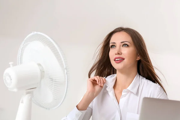 Young woman using electric fan during heatwave in office — Stock Photo, Image