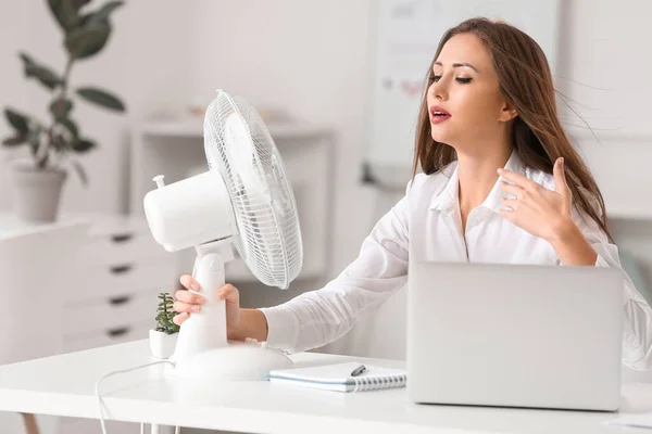 Mladá žena pomocí elektrického ventilátoru během horké vlny v kanceláři — Stock fotografie