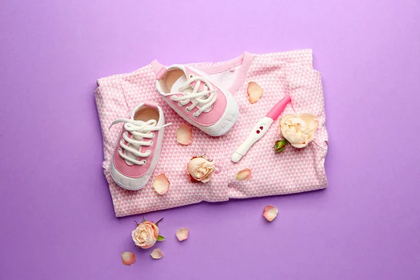 stock image Pregnancy test, baby clothes and flowers on color background