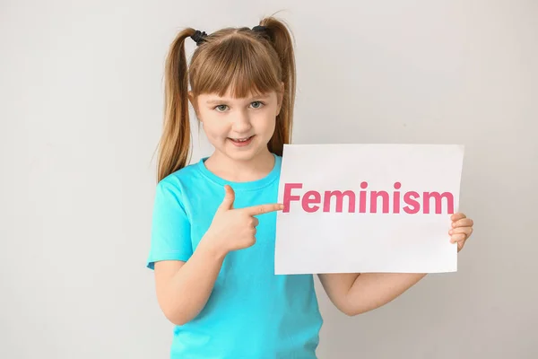 Klein meisje met papier met woord feminisme op lichte achtergrond — Stockfoto