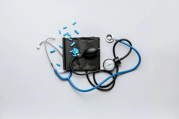 Blutdruckmessgerät und Pillen auf hellem Hintergrund — Stockfoto
