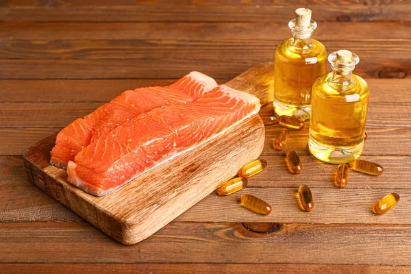 Fish with oil and pills on wooden background — Stock Photo, Image