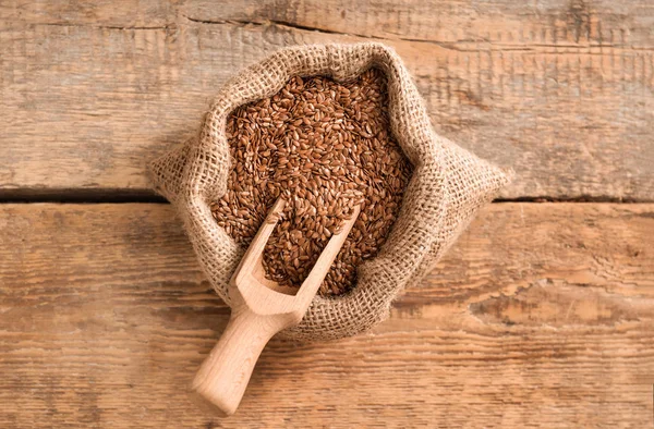 Bag with flax seeds and scoop on wooden background — Stock Photo, Image