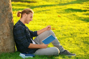 Dışarıda kitap okuyan yakışıklı bir adam.