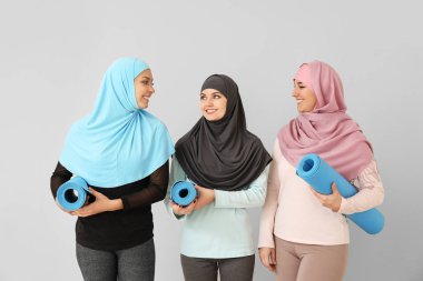 Hafif arka planda yoga minderleri olan sportif Müslüman kadınlar.
