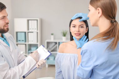 Klinikte ameliyattan önce genç bir kadının yüzünü muayene eden bir plastik cerrah.