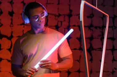 Siyah arka planda, kulaklık ve neon lambalı Afro-Amerikan bir adamın tonlu portresi.