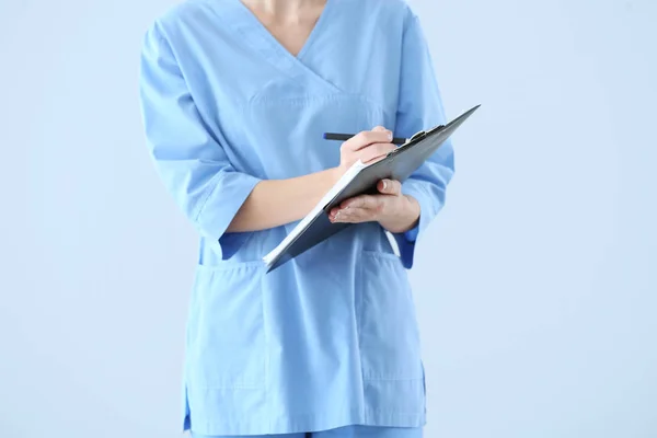 Female doctor with clipboard on light background — Stock Photo, Image