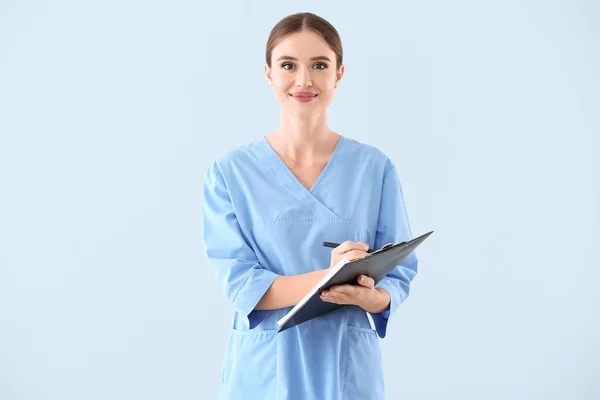 Portrait of female doctor with clipboard on light background — Stock Photo, Image