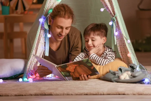 Padre y su pequeño hijo leyendo el libro por la noche en casa —  Fotos de Stock