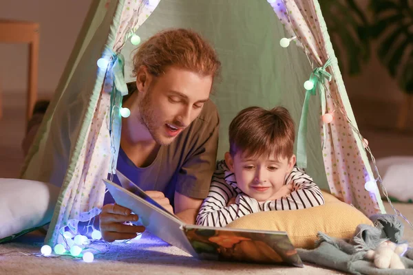 Father and his little son reading book in evening at home — Stock Photo, Image