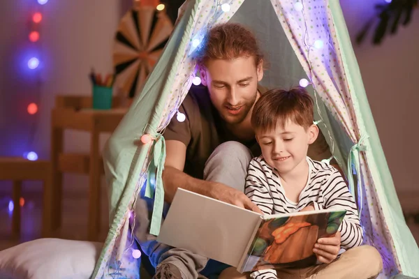 Padre y su pequeño hijo leyendo el libro por la noche en casa — Foto de Stock