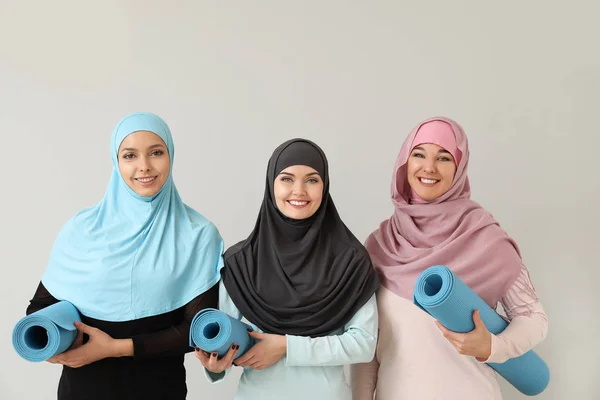 Mulheres muçulmanas desportivas com tapetes de ioga no fundo claro — Fotografia de Stock