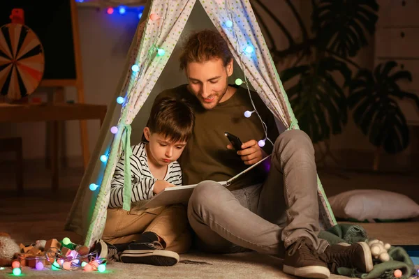 Father and his little son reading book at home in evening — Stock Photo, Image